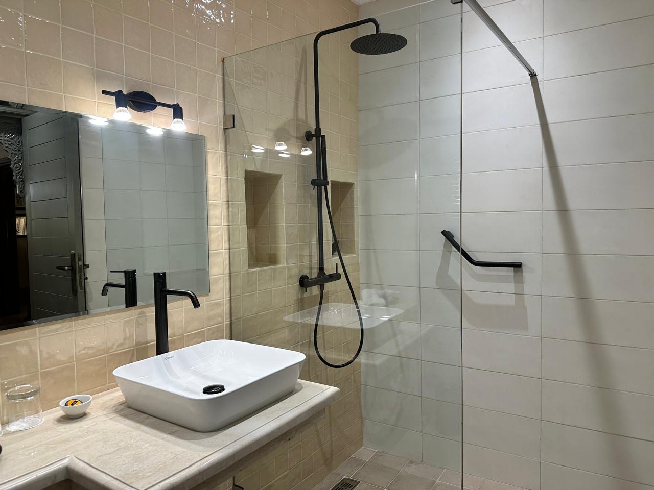 A bathroom with a walk-in rain shower behind glass, black fittings and a stone basin