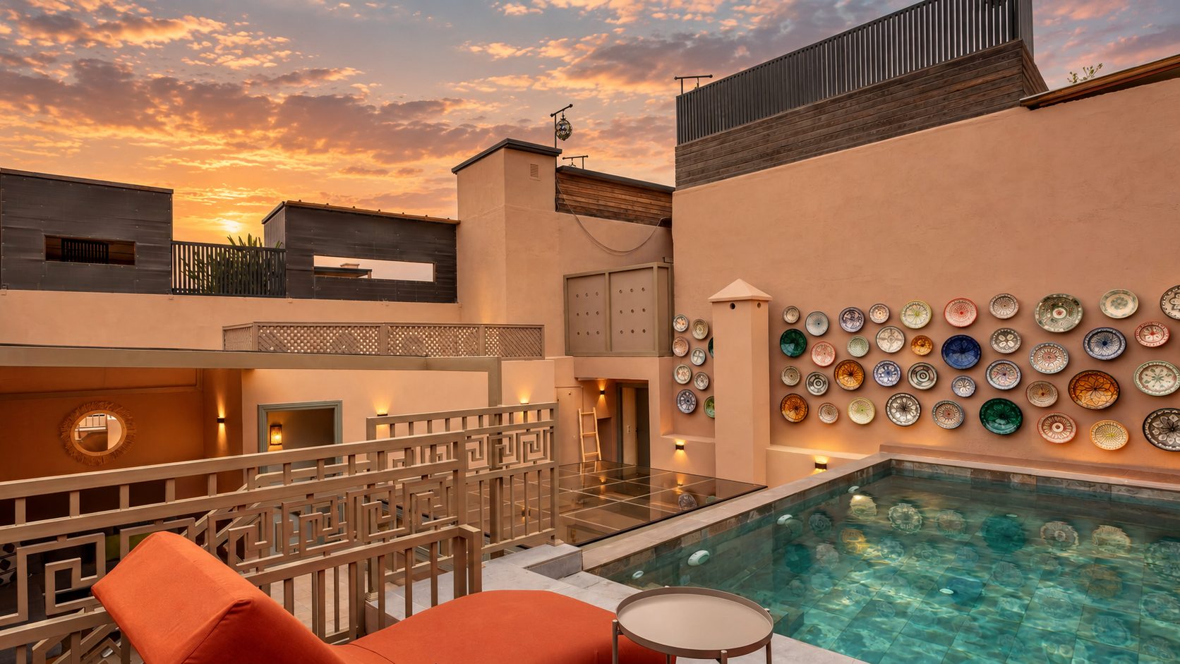 The rooftop terrace at sunset: the pool, the wall of hand-painted plates and the loungers beneath a golden sky