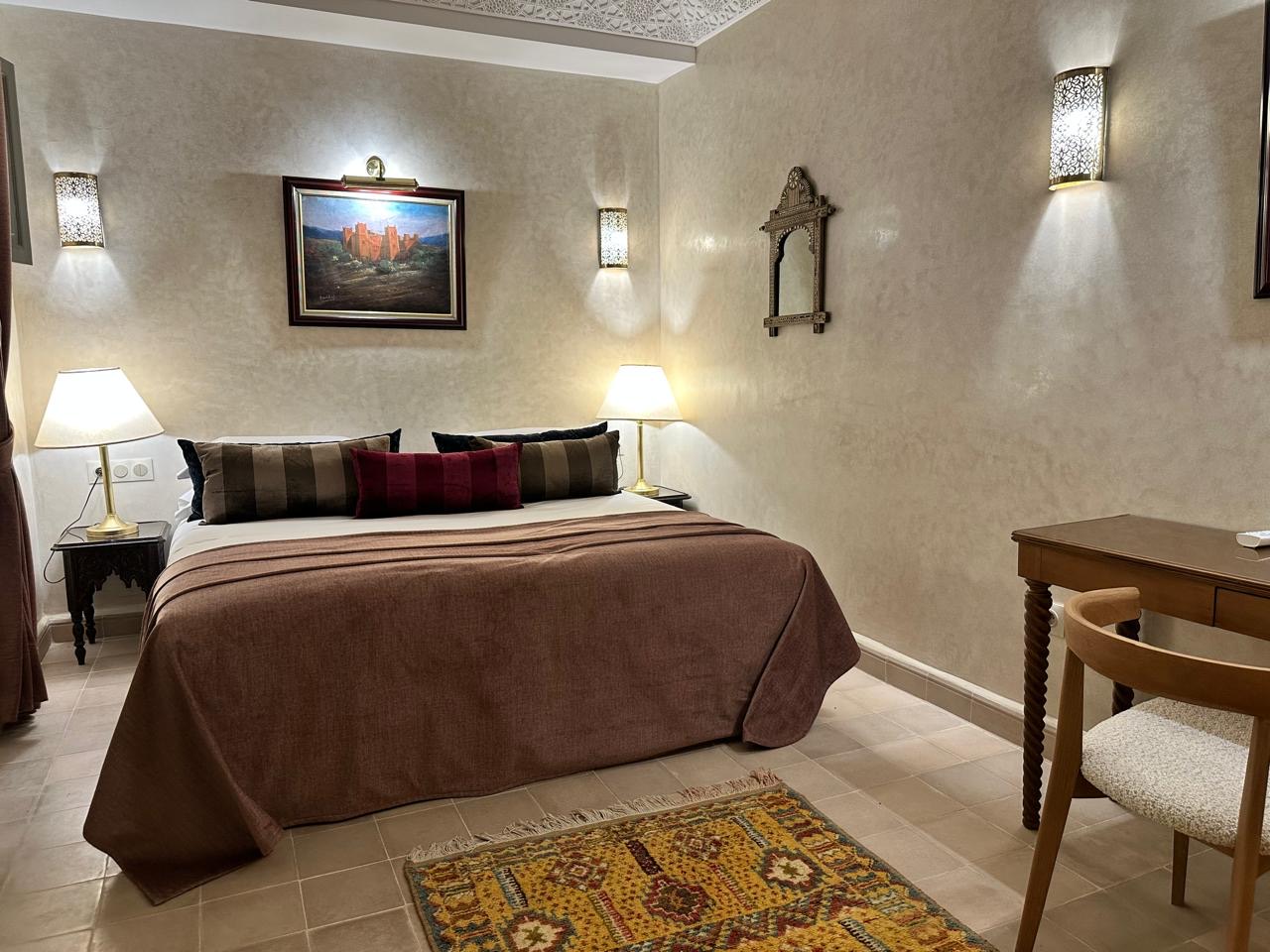 A bedroom with a king bed, lantern sconces and a writing desk